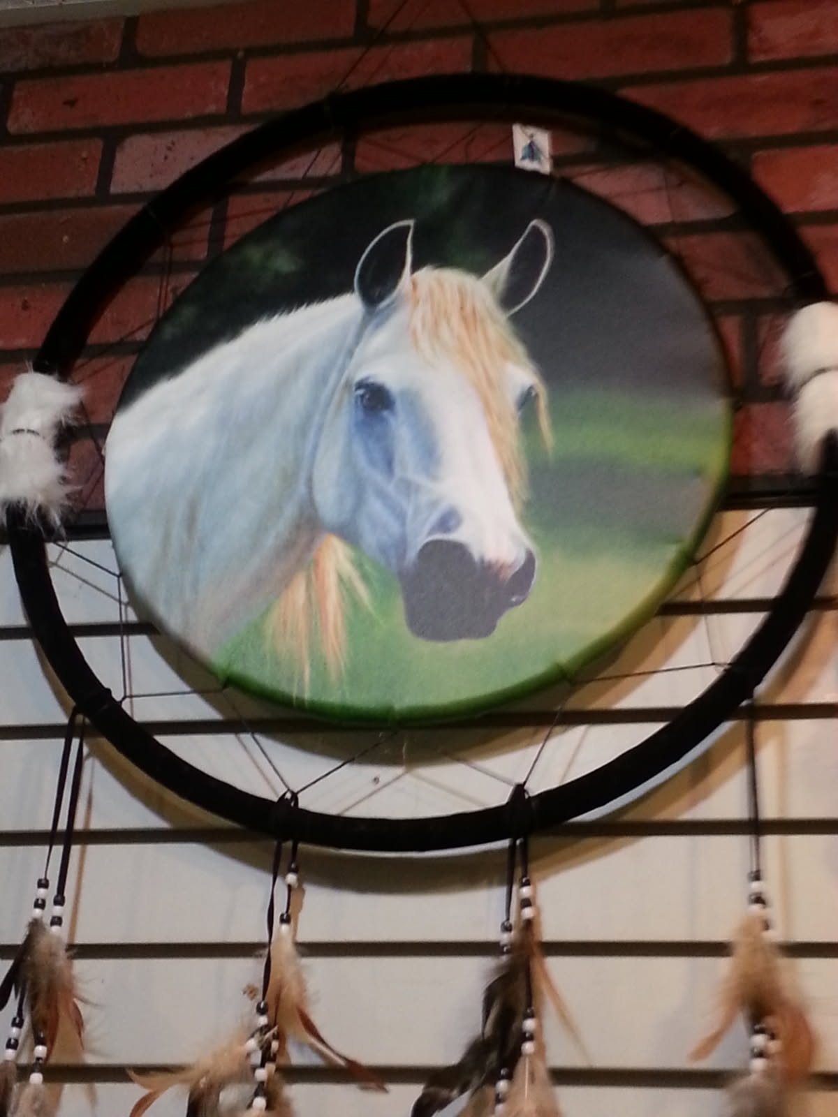 Dream catcher painted with a white horse in a green pasture, hung on a brick wall