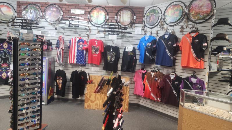 Store corner with graphic T-shirts and polos, a sunglasses rack, and dream catchers on the wall above