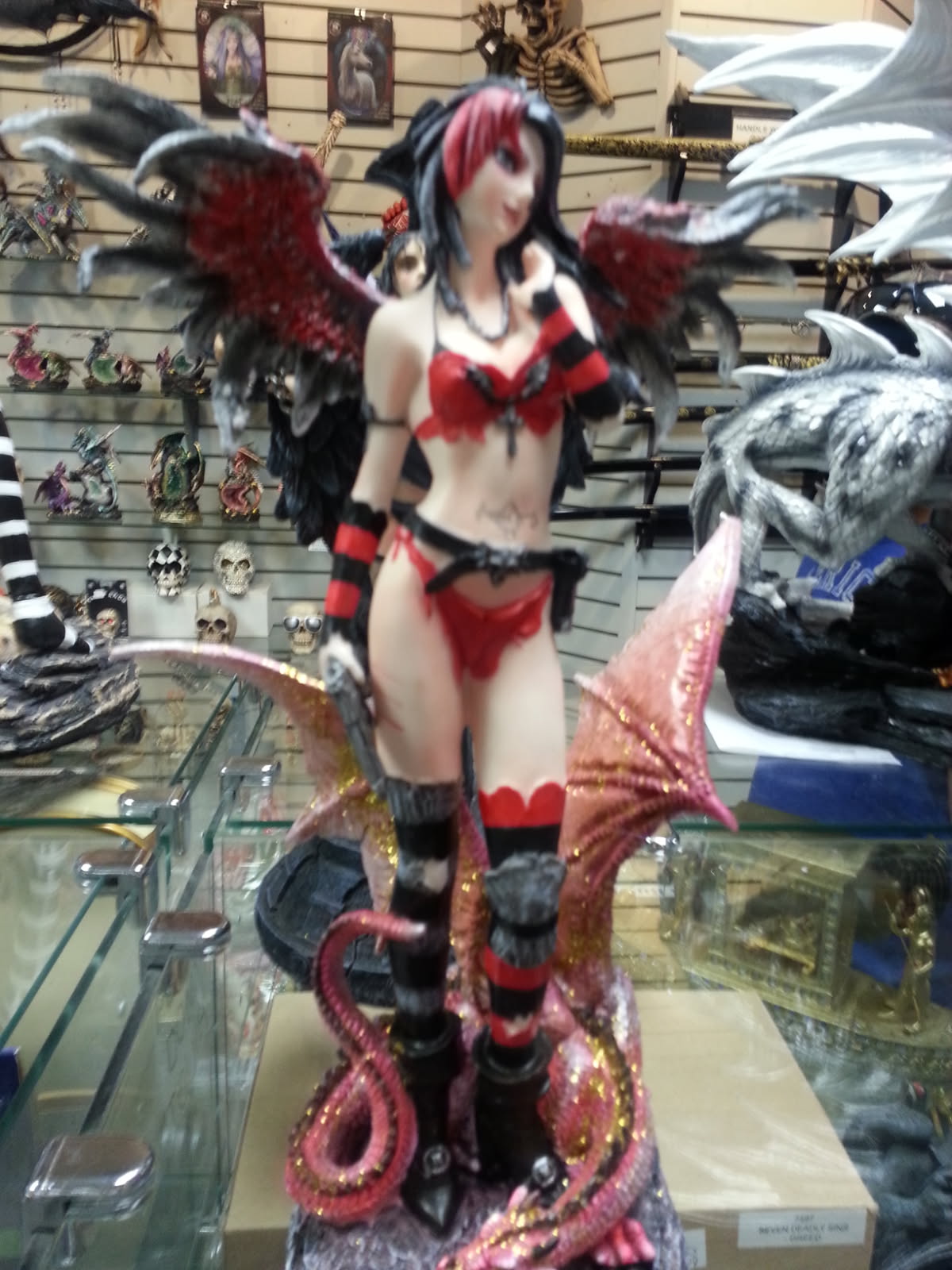 Gothic winged fairy figurine in red and black on a glass counter among dragon and skull collectibles