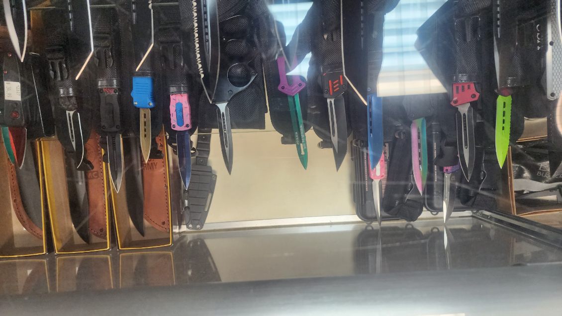 Display case of fixed blades in leather sheaths beside brightly coloured tactical folding knives