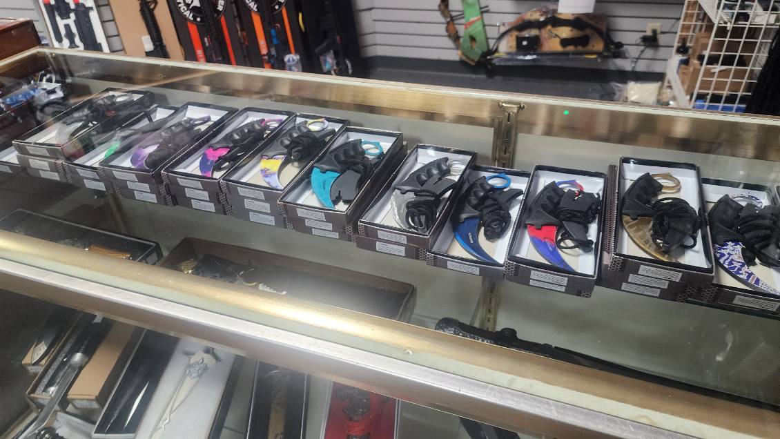 Row of boxed karambit knives with ringed handles in assorted colours inside a glass counter