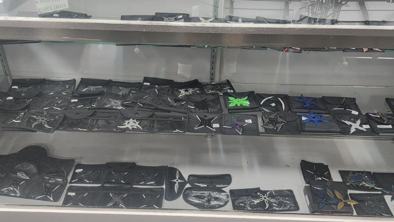 Display shelves of throwing stars in black carrying pouches, several in coloured finishes