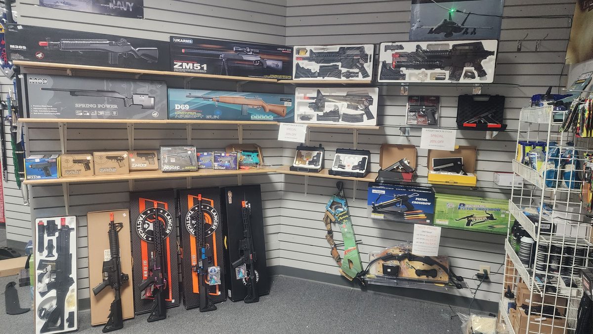 In-store wall display of boxed airsoft rifles, pistols, and pistol crossbows on slatwall shelving