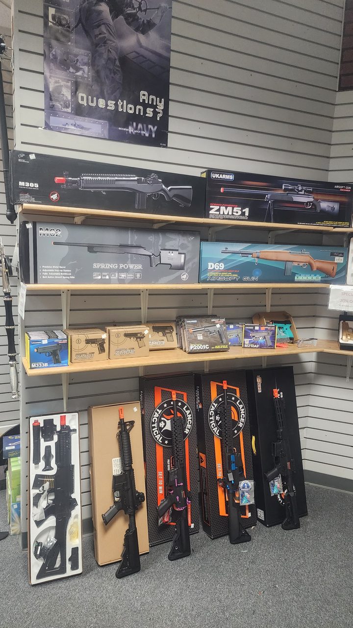 Shelves of boxed airsoft rifles and pistols above rifles standing on the floor