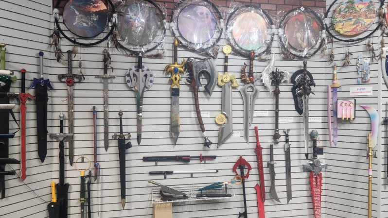 Slatwall hung with anime and video game replica swords and axes beneath a row of dream catchers