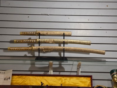 Three katanas with gold-wrapped handles and matching scabbards on a tiered display stand