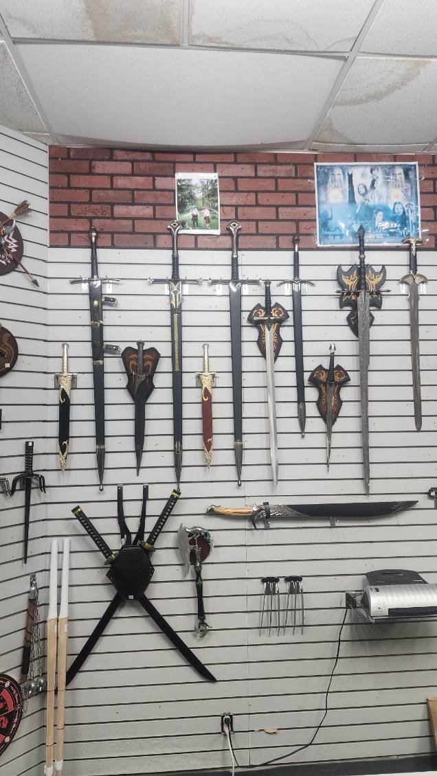 Corner wall of broadswords, daggers and plaque-mounted fantasy blades above crossed ninja swords and throwing knives