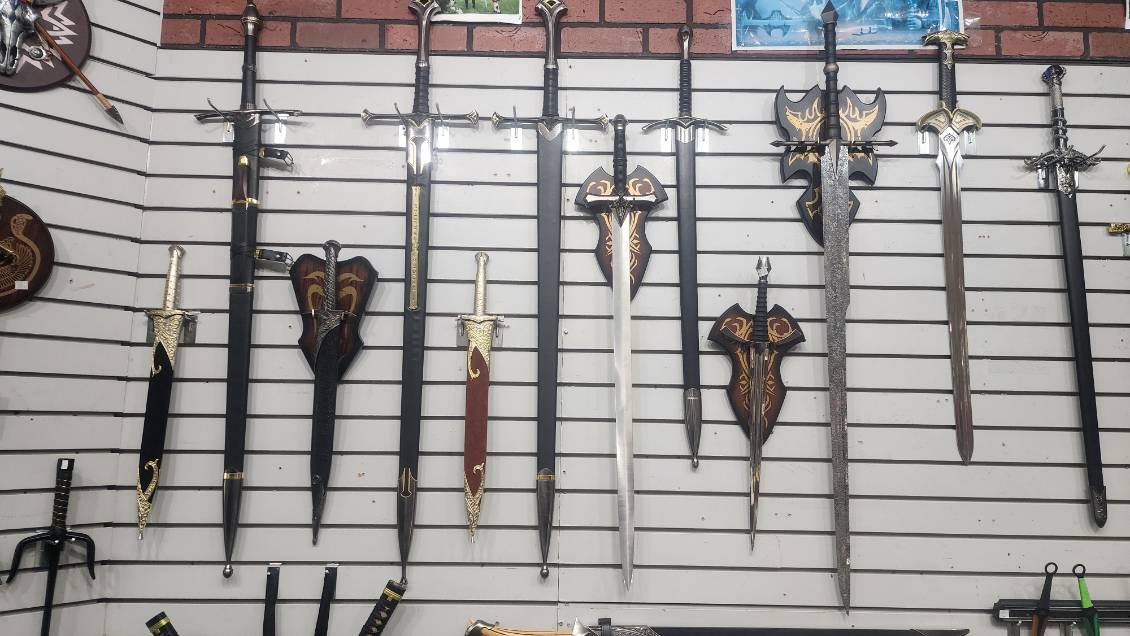 Row of medieval and fantasy broadswords and daggers on a slatwall, several mounted on carved display plaques